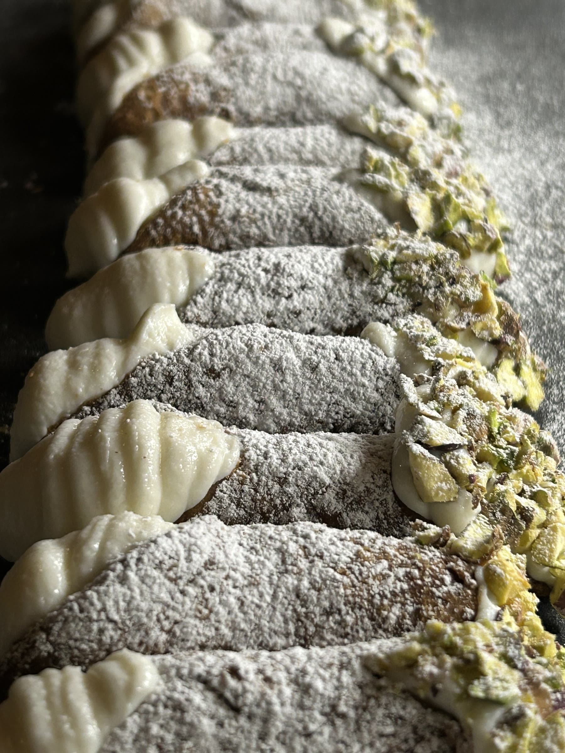 Rad av cannoli, krispigt skal doppat i florsocker och hackad pistage.