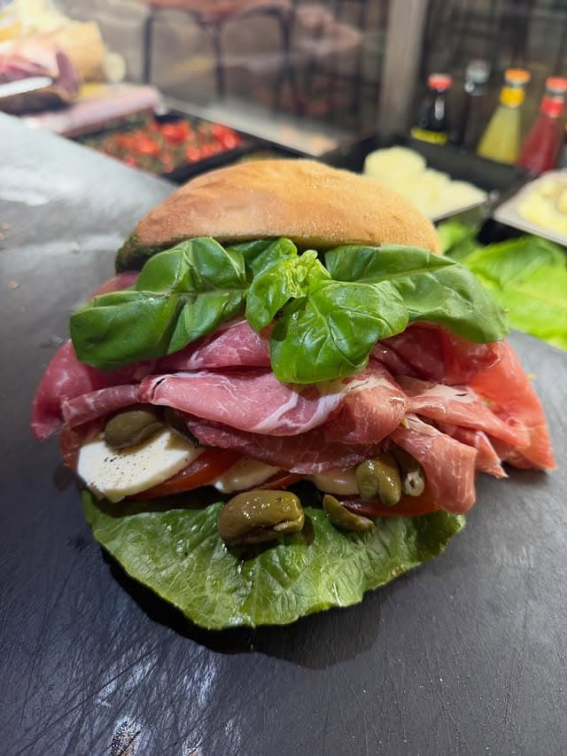 Smörgås med capicollo, mozzarella, tomat och basilika på en skifferbricka.