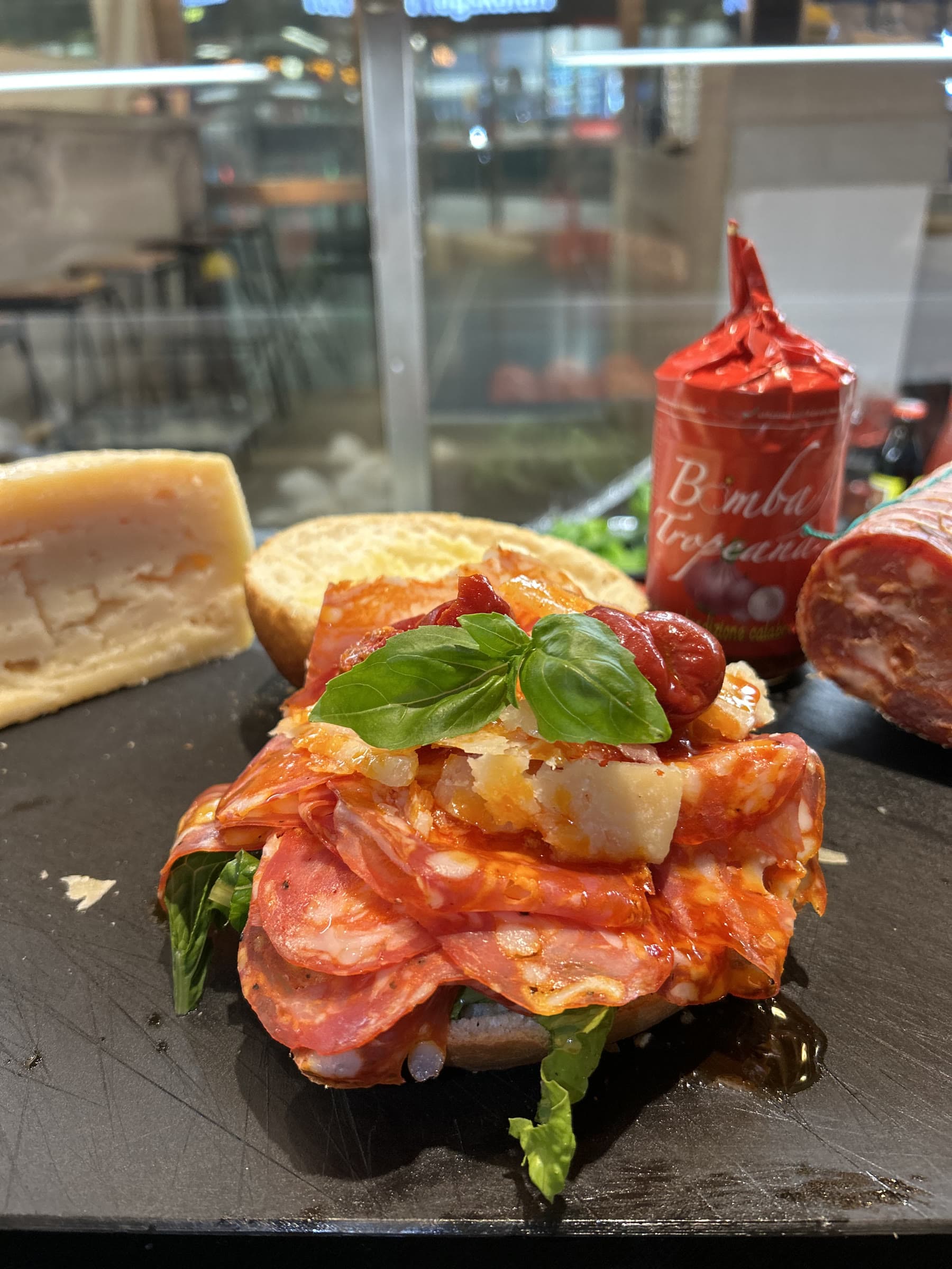 Smörgås bredvid en parmigianokil, salame och en burk Bomba Tropeana.