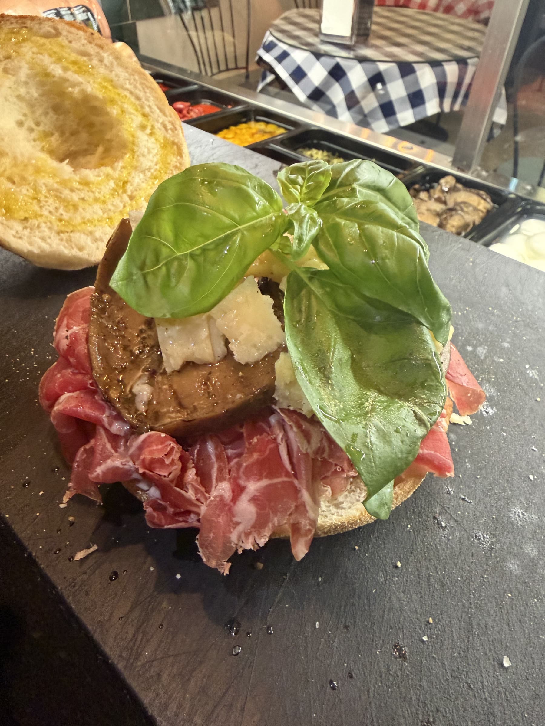Smörgås med prosciutto, en skiva grillad aubergine, hyvlad ost och basilika, precis byggd.