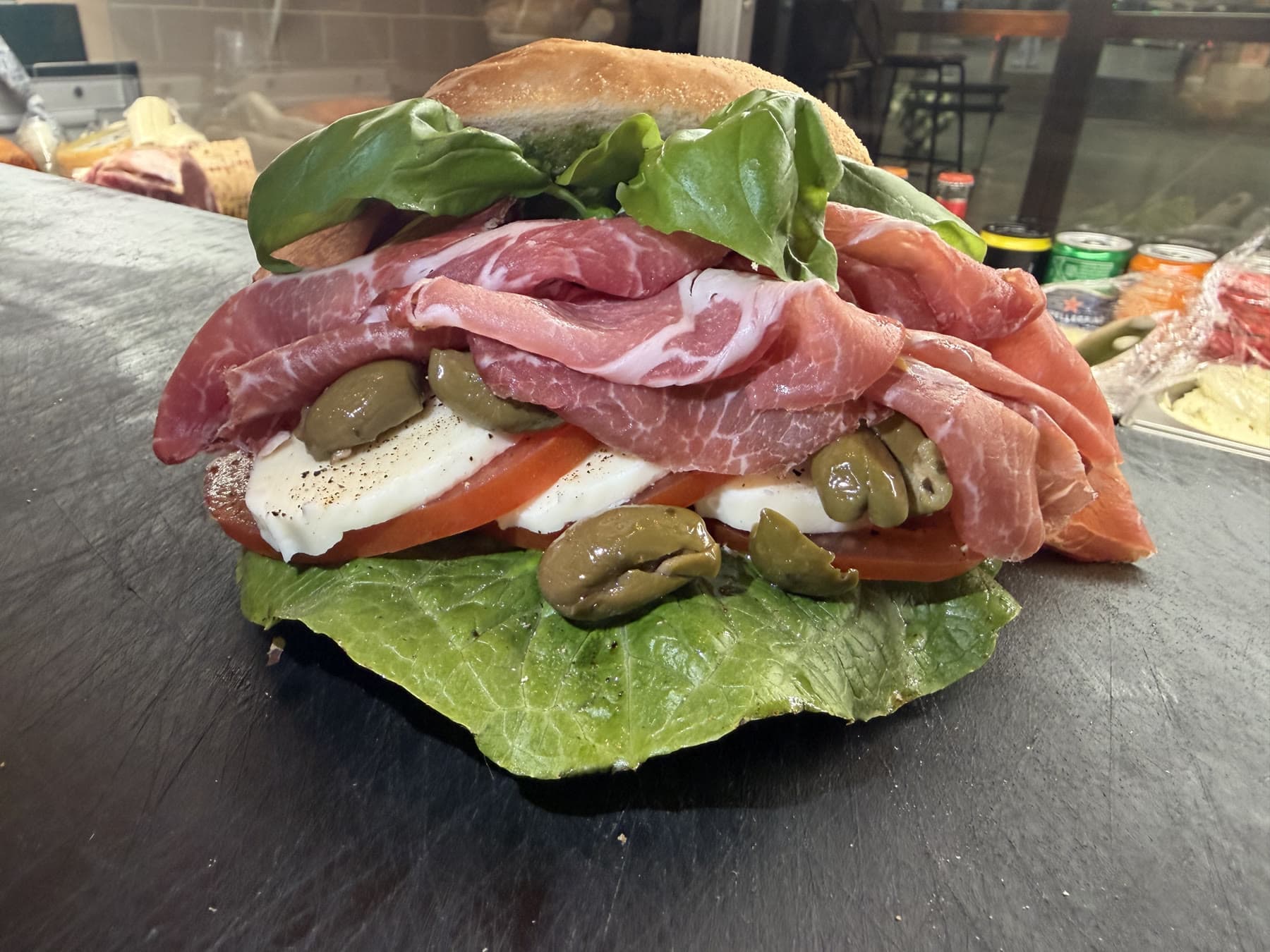 En smörgås med skinka, mozzarella, tomat, gröna oliver och basilika, nybyggd på disken.